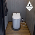 Load image into Gallery viewer, Cinderella Premium incineration toilet in a bathroom with wooden floor and gray walls, featuring a brand logo.