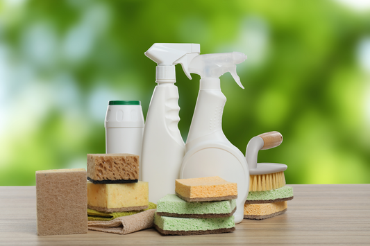 Cleaning supplies including bottles, sponges, and scrubbers on a wooden surface with a green blurred background.