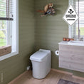 Load image into Gallery viewer, Bathroom with green walls, a Cinderella Freedom incineration toilet, and a vanity unit with a window in the background.
