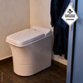 Load image into Gallery viewer, Cinderella Freedom incineration toilet in a bathroom with a dark bathrobe hanging on a hook.
