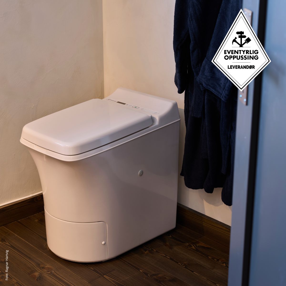 Cinderella Freedom incineration toilet in a bathroom with a dark bathrobe hanging on a hook.