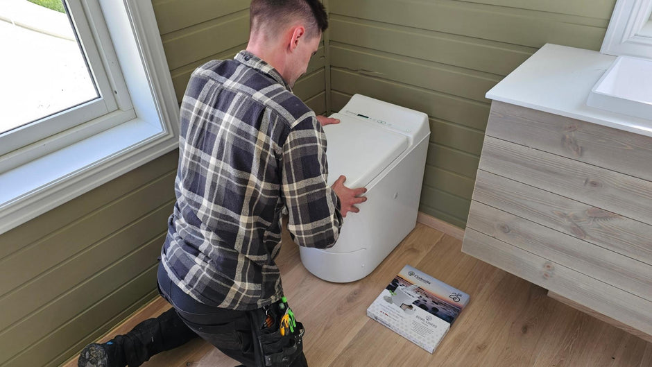 Person installing a Cinderella Freedom incineration toilet in a bathroom setting