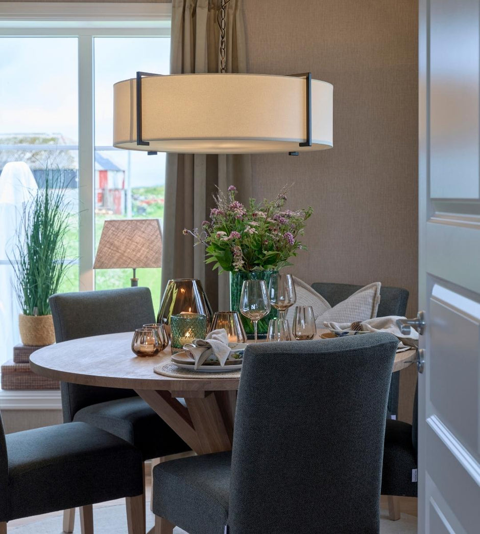 Dining room with a round table set for a meal, featuring chairs, a lamp, and decorative elements.
