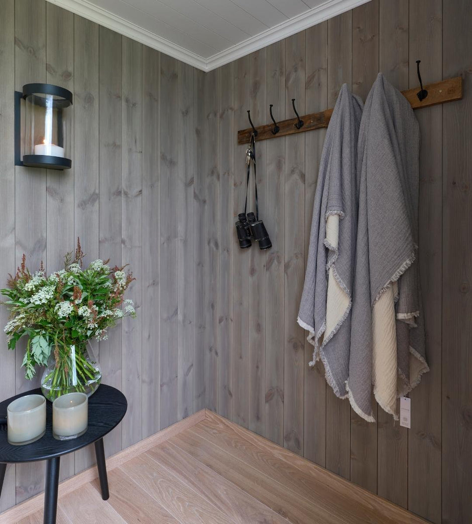 Wooden wall with hooks, a vase of flowers, and candles on a small table.