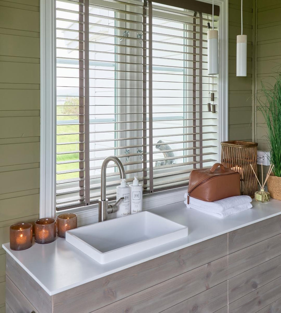 Bathroom vanity with sink, candles, and towels near a window with blinds.