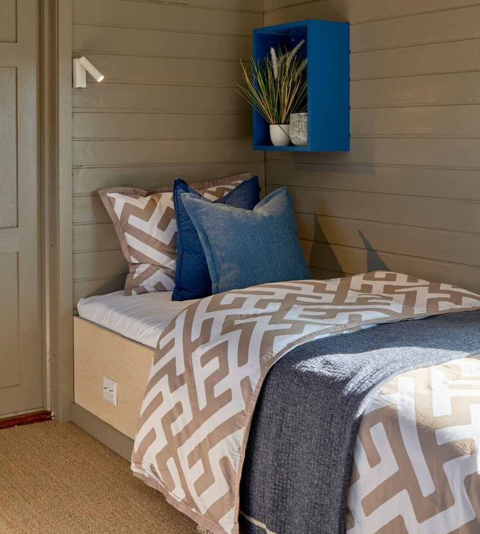 Bed with patterned bedding and blue pillows in a room with wooden walls and a blue shelf.