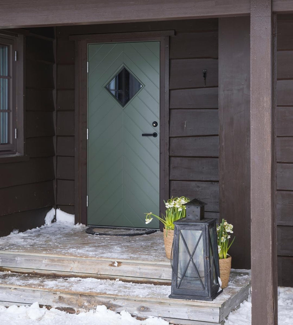 Green door with diamond-shaped window on a wooden porch with snow.