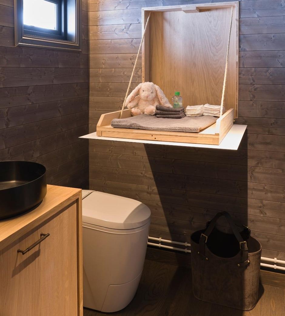 Bathroom with wooden shelf above the incineration toilet, containing towels and a bottle.