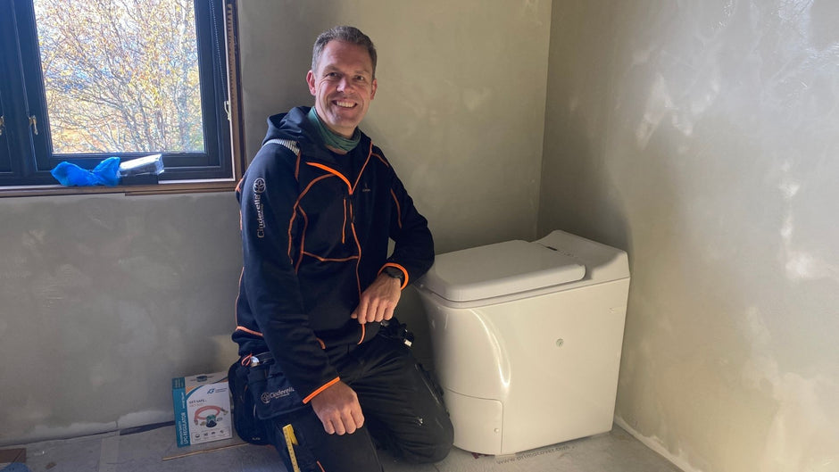 Man kneeling next to a Cinderella toilet in a room with unfinished walls.