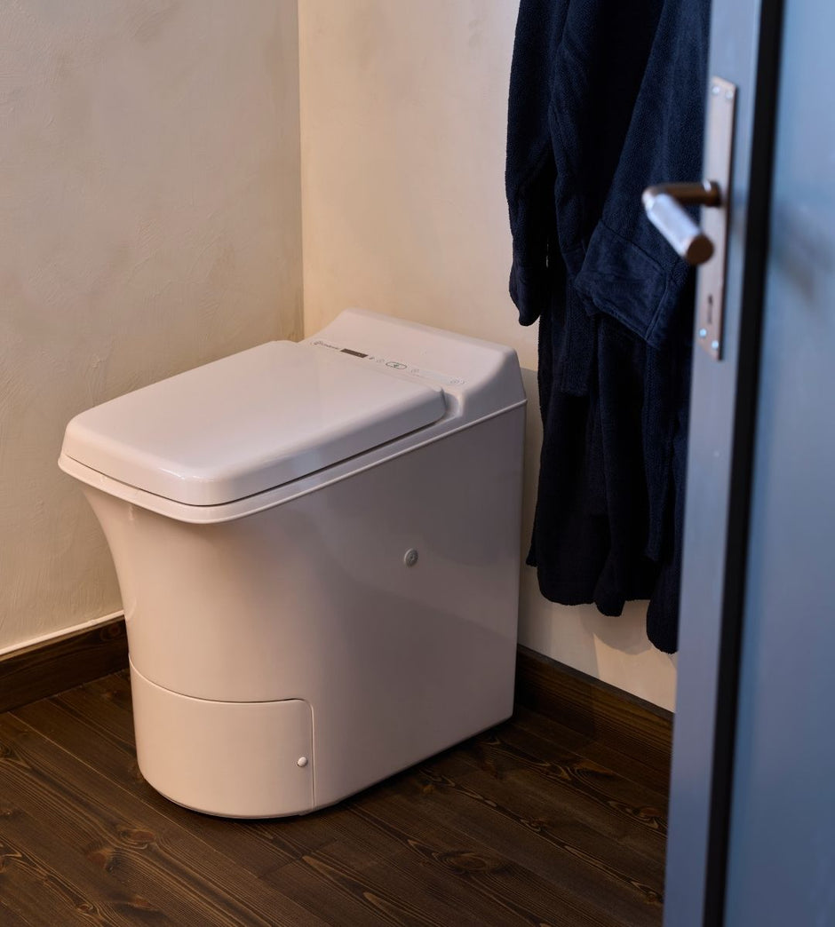 Cinderella Freedom incineration toilet against a beige wall with a dark robe hanging on a hook.