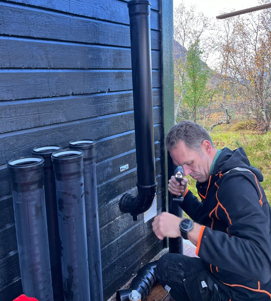 Person installing a black ventilation pipe against a wooden wall with a scenic background