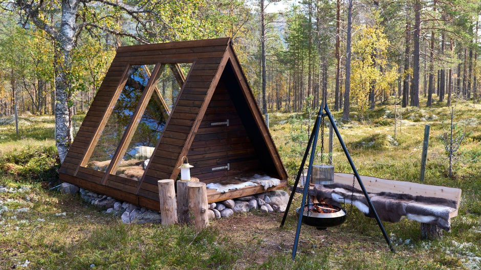 Trästuga i en skog med en eldstad och en sittgrupp.