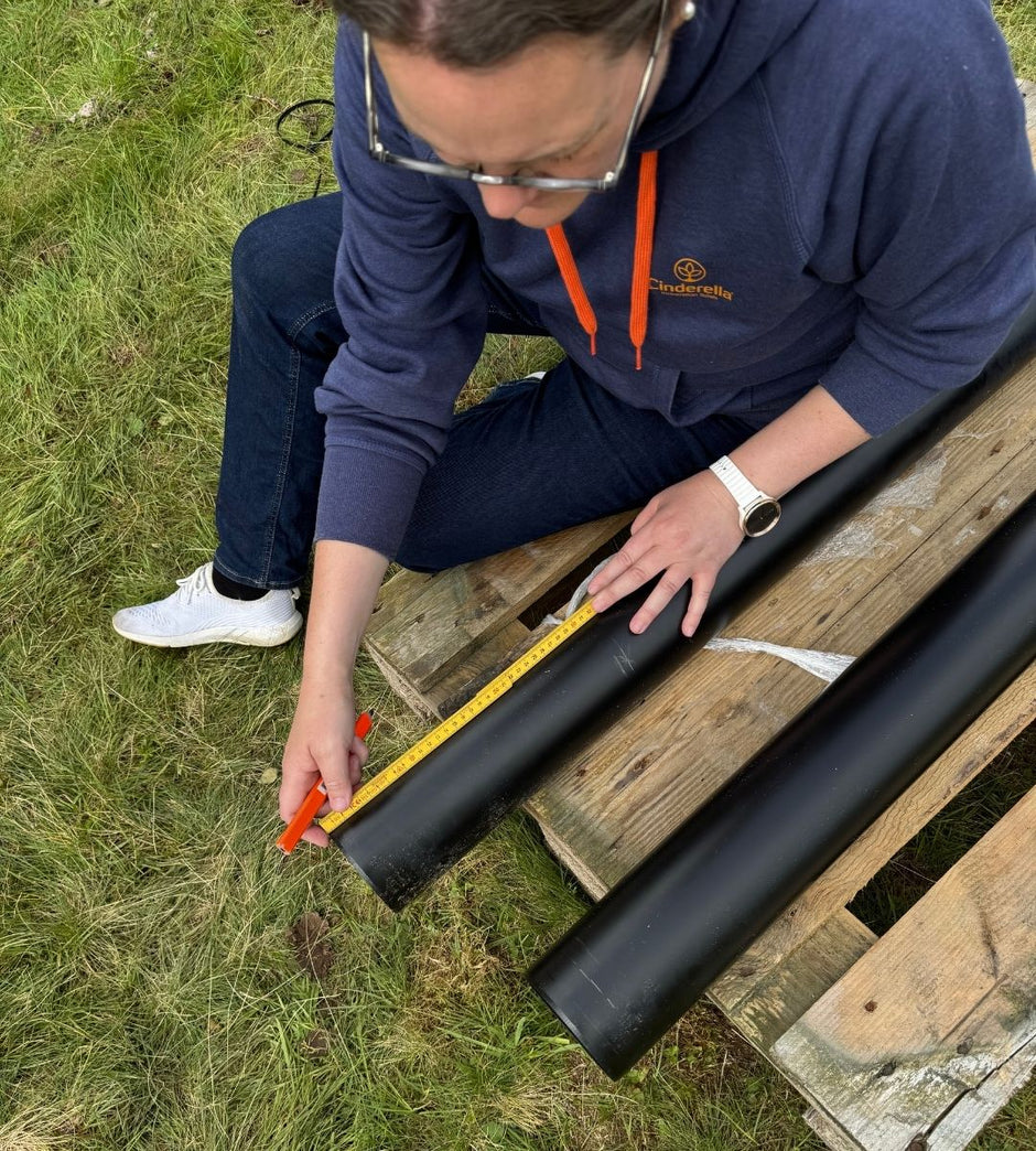 Person som mäter ett svart rör på en träpall utomhus
