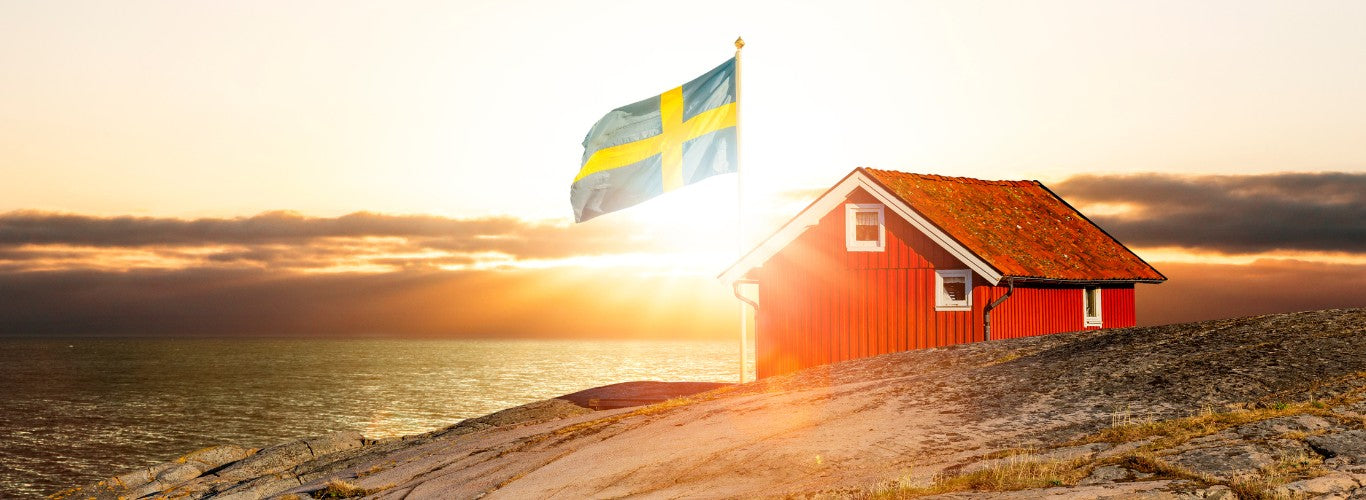 Röd stuga på en klippa med en svensk flagga vid solnedgången